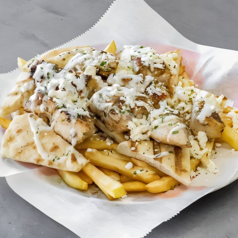 Chicken souvlaki with pita bread, fries, white sauce, and feta cheese in a paper-lined basket.