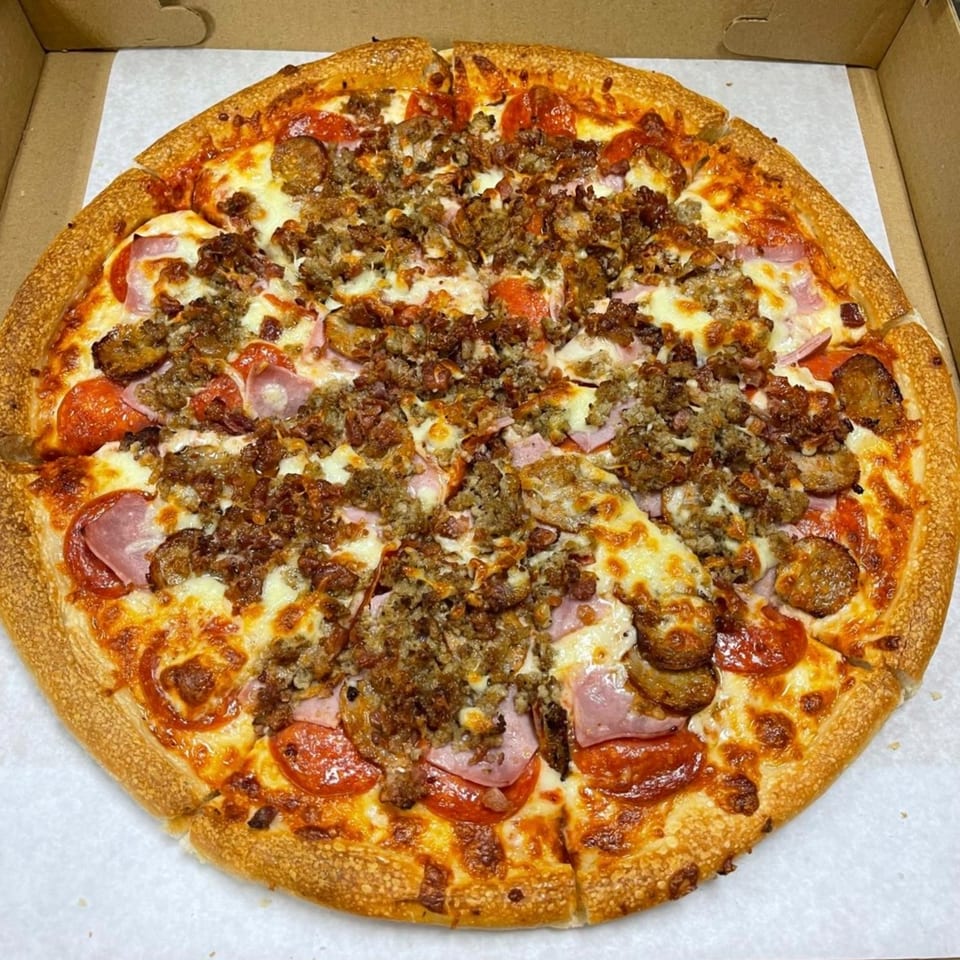A Family Style Pizza with pepperoni, ham, sausage, and ground beef in a cardboard box.