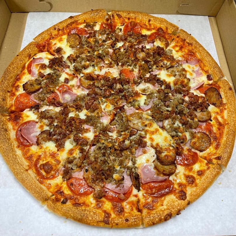 A Family Style Pizza with pepperoni, ham, sausage, and ground beef in a cardboard box.