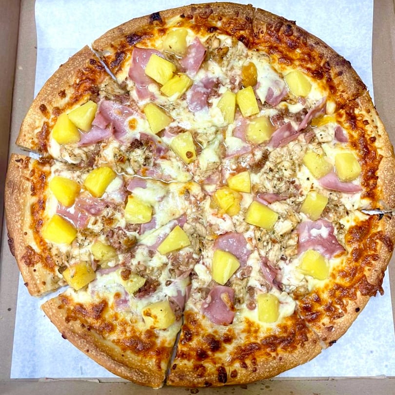 A Family Style Pizza with pineapple, ham, and chicken, sliced and ready to eat.